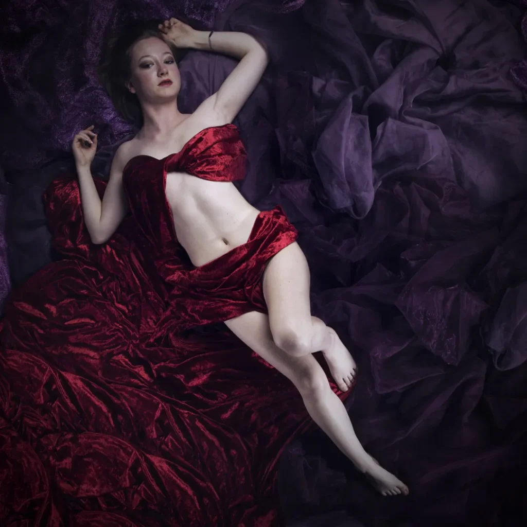 a woman lying on a bed wearing a red dress