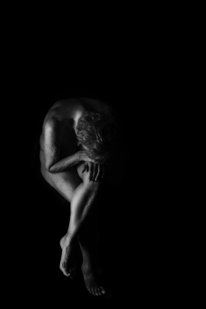 a naked man sitting on a black background